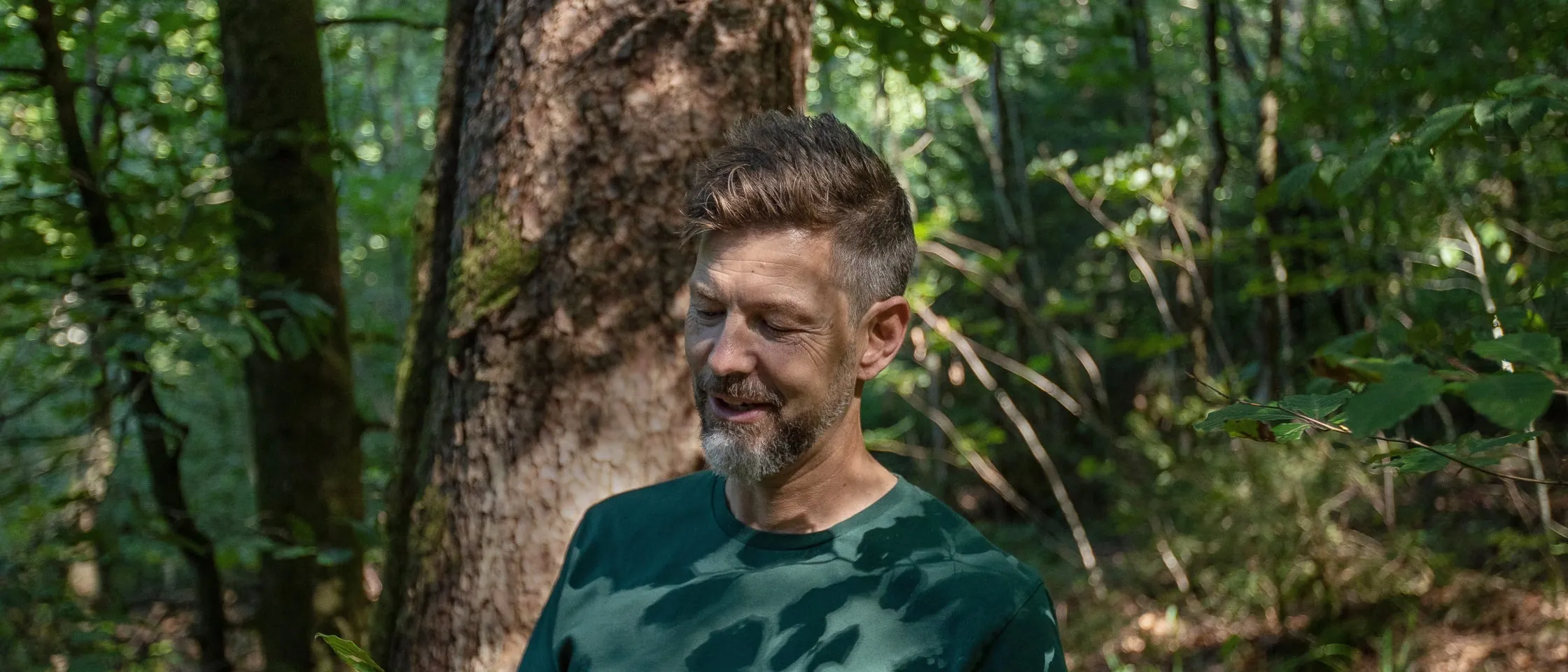 Jodok Batlogg in a forest, looking down and smiling.